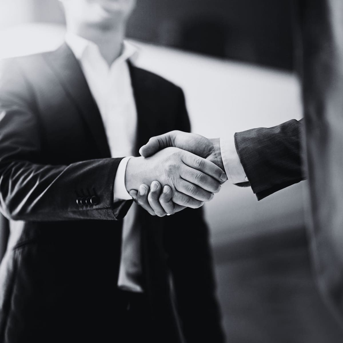 Apretón de manos entre dos personas de traje, en blanco y negro